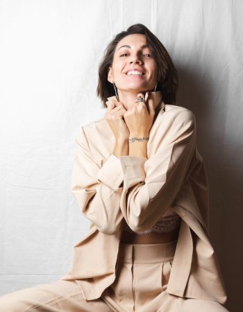 gentle-portrait-beautiful-young-woman-with-big-breasts-beige-suit-white-lace-bra-sits-chair-gray-white_343596-3214